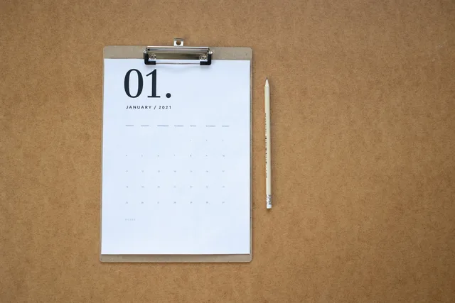 Flat lay of a January 2021 calendar on a clipboard with a pencil on brown background. A checklist for marketing attribution tool implementation